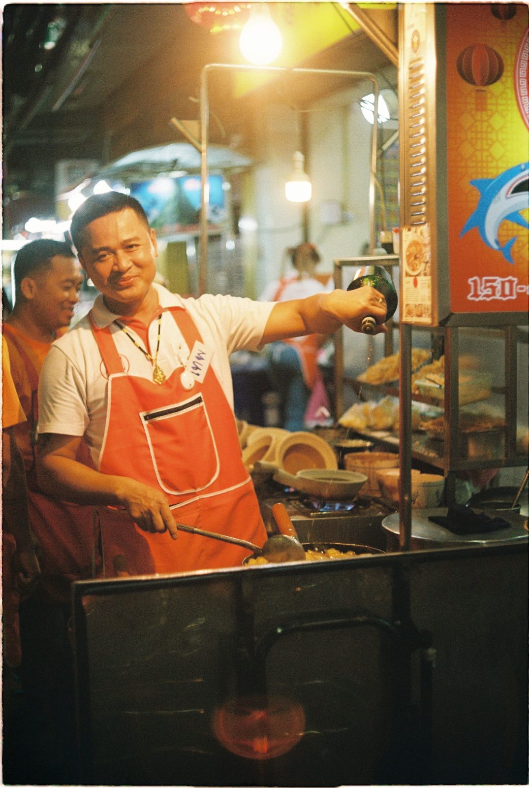 A street-food cook looks ahead with focus while working at the stove.
