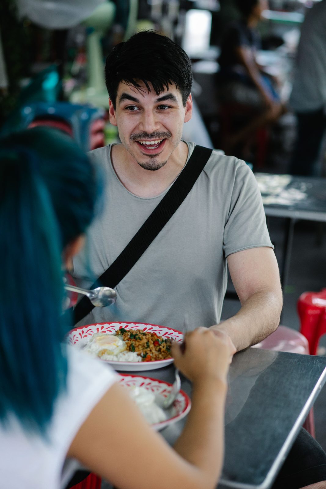 A smiling customer eats pad kra pao with friends at a street-side restaurant.