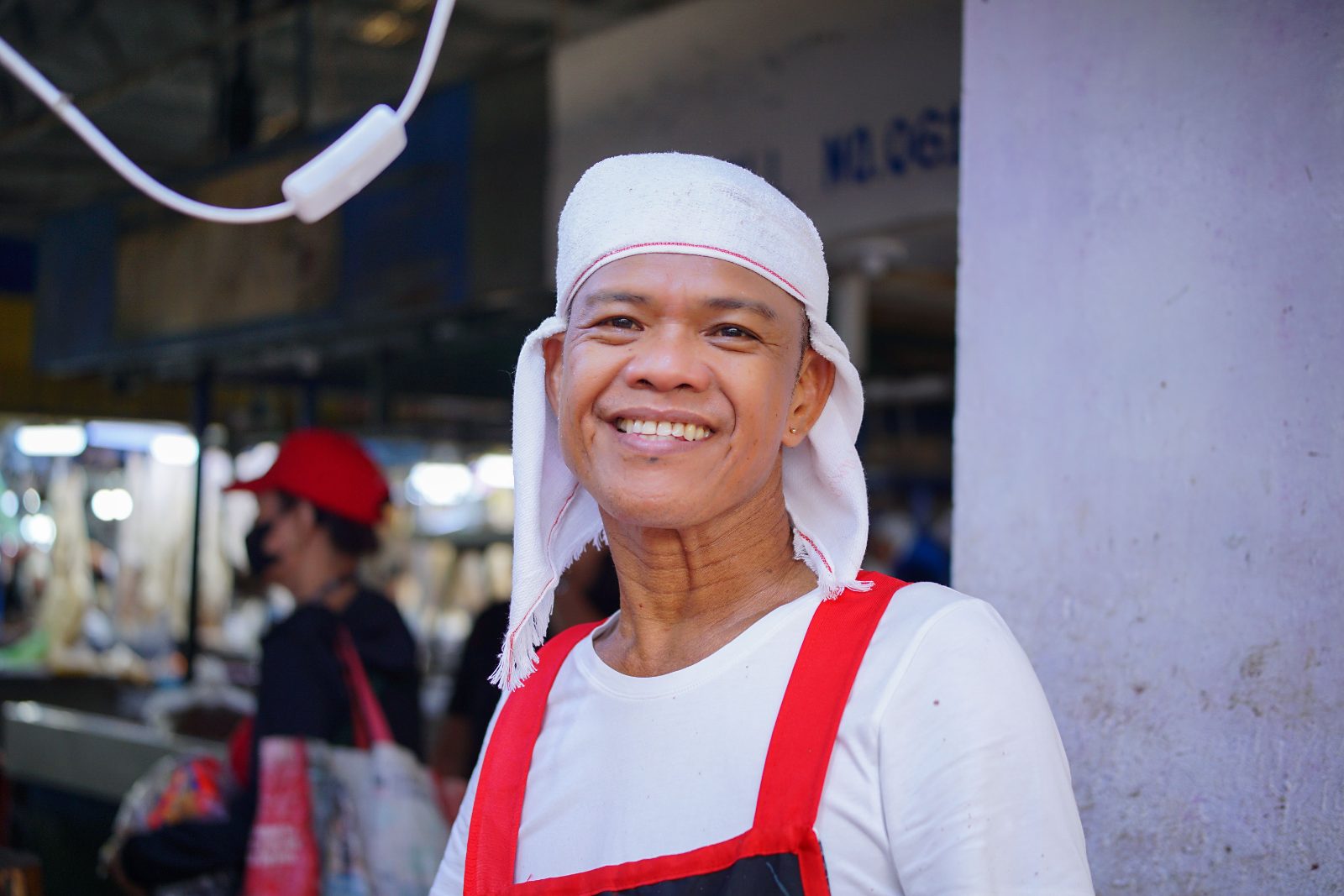 A market vendor in a headscarf smiles broadly in front of his stall.